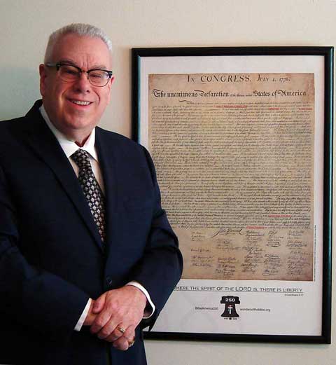 Frank DeFreitas stands next to his semiquincentennial re-creation of the Declaration of Independence. The phrases referencing God have been highlighted.